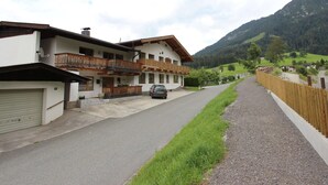 A two-story chalet with a balcony, a car parked in front, and a gravel driveway leading to a wooden fence. - Boutique Apartment With Mountain View (Brixen im Thale)