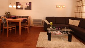 A living room with a dark brown sofa, a glass coffee table, and a dining area with a wooden table and chairs. - Boutique Apartment With Mountain View (Brixen im Thale)