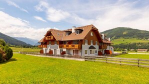 A large, two-story wooden house with a balcony, surrounded by a wooden fence and green fields. - Welcoming Apartment in Sankt Margarethen im Lungau near Ski Area (Sankt Margarethen im Lungau)