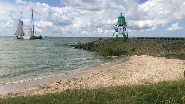 Une plage avec un phare et des voiliers à l’horizon.
