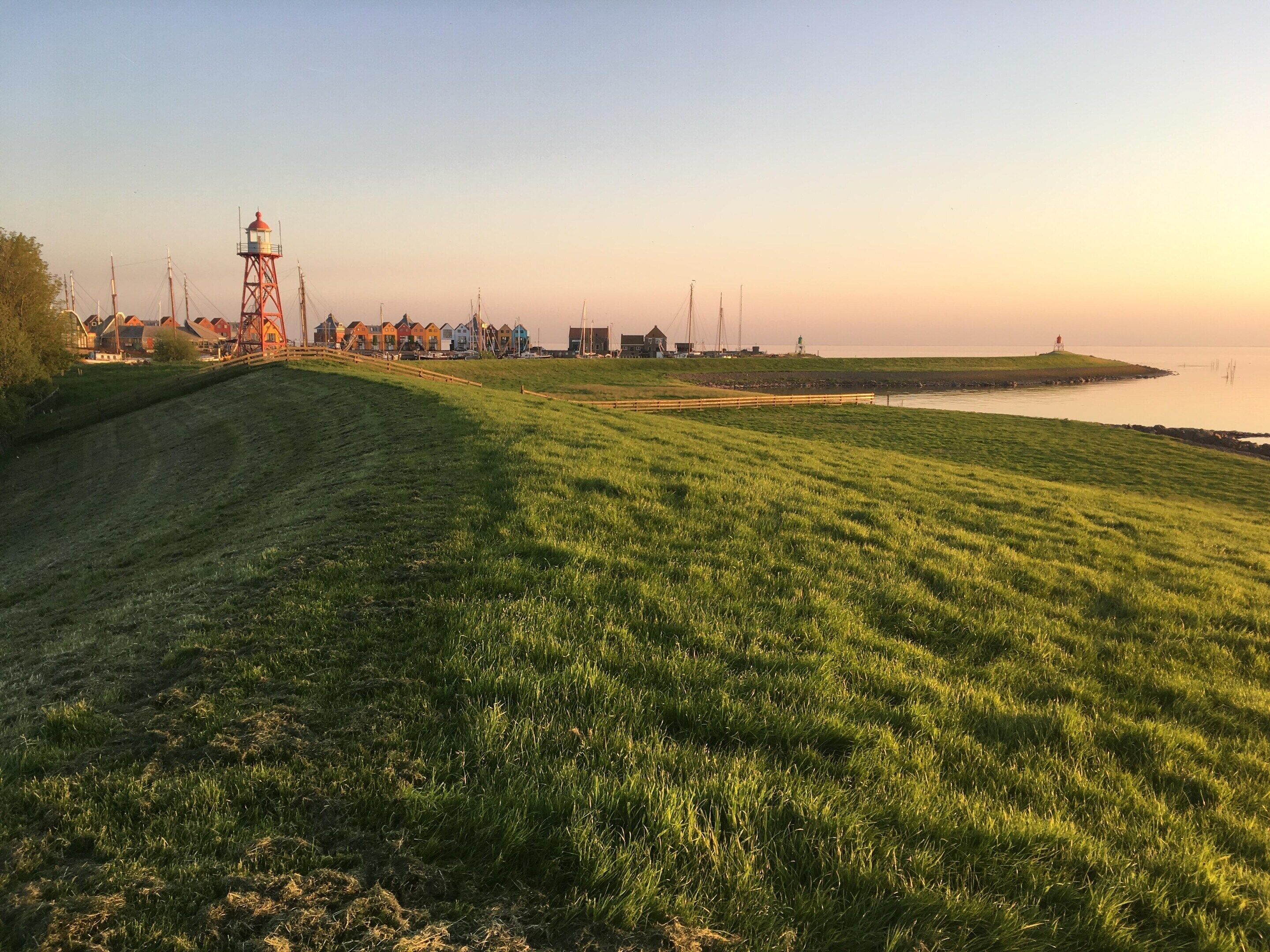 Un paisaje costero con un faro, campos cubiertos de hierba y un mar tranquilo.