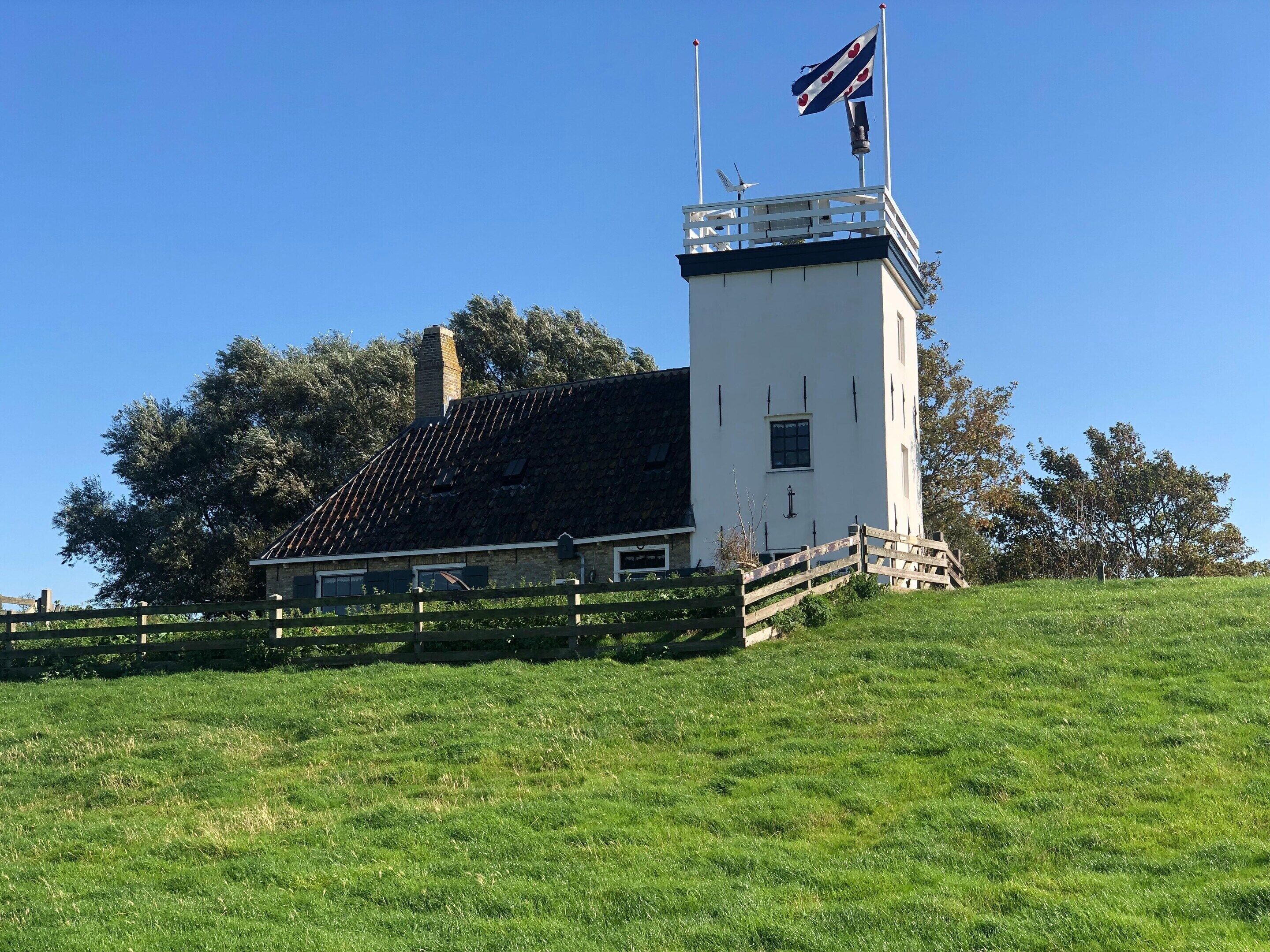 A white tower with a flag, a wooden fence, and a grassy hill.