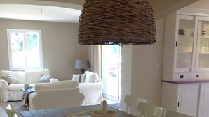 Un comedor con una mesa de madera, sillas blancas, una lámpara colgante de fibra y vistas a un balcón con un sofá blanco.