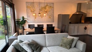 Ein modernes Wohnzimmer mit grauem Sofa, einem Esstisch mit Stühlen, einer großen Weltkarte an der Wand und einer Küchenzeile im Hintergrund.