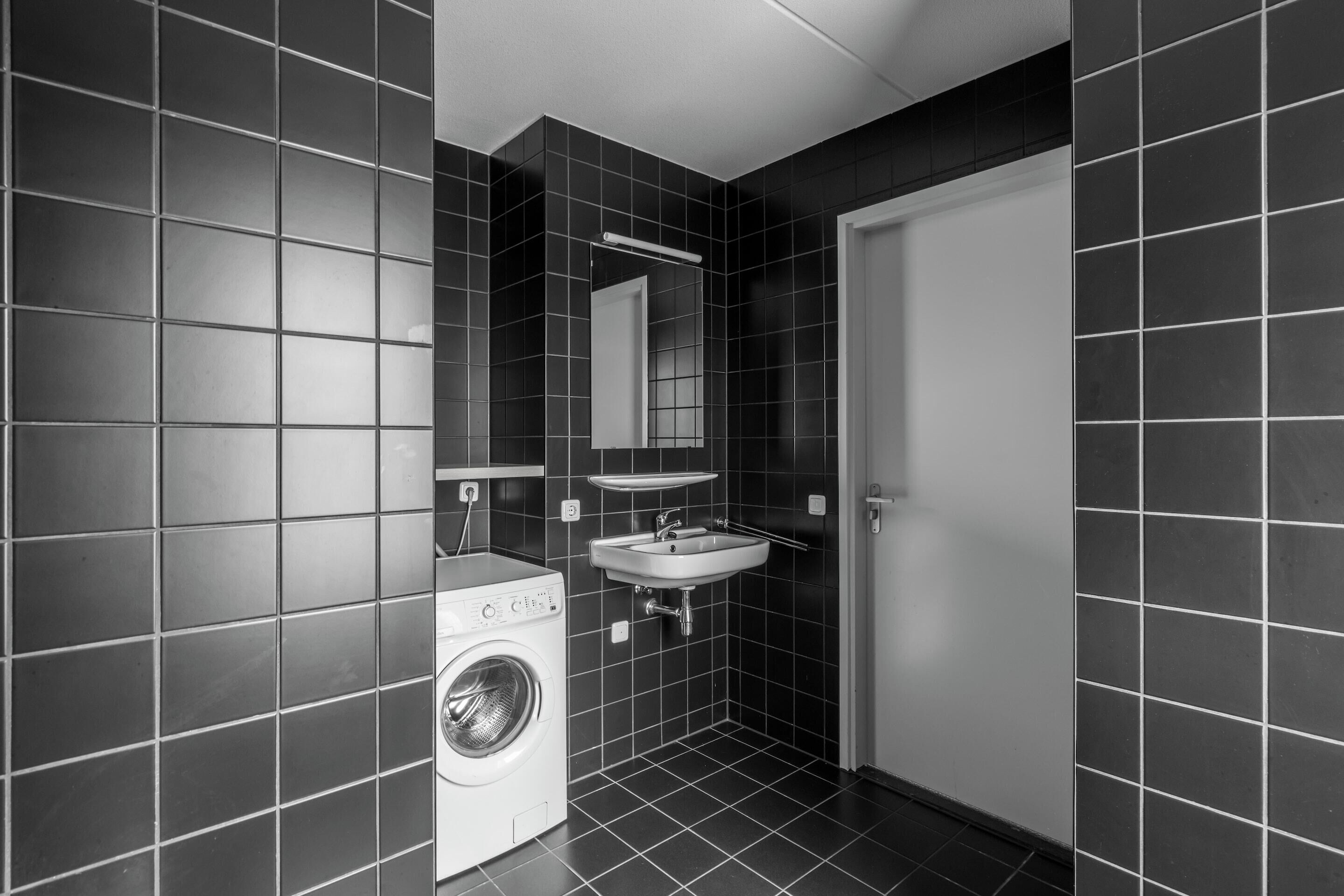 A compact, modern bathroom with a washing machine, a sink, and a mirror.