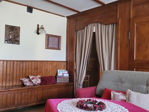 A room with wooden paneling, a bed with a pink bedspread, a grey sofa, a wooden bench, and a wall with framed items. - Holiday Home Alsace Near Vosges Nature Park (Schleithal)