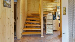 Un interior de madera con una escalera, piso de baldosas y una estantería.