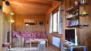 A wooden cabin interior with a sofa, a television, and shelves with books and decorations. - Chalet in Saulxures Near Ski Resorts (Saulxures-sur-Moselotte)