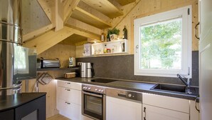 Ett modernt kök med träbjälkar, en inbyggd ugn, en kaffebryggare och ett fönster med utsikt över grönskan.