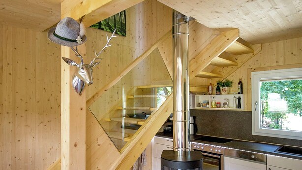 Ett modernt kök med en vedeldad kamin, en spiraltrappa i glas och utsikt över omgivningarna.
