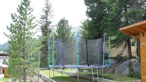 Un trampolín en un patio trasero con una valla de madera, árboles y un edificio pequeño.