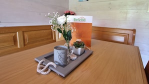 Une table en bois ornée d’un vase de fleurs, d’une bougie et d’une petite plante. On peut voir, au fond, une enseigne portant le nom « Belvilla ».