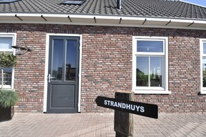 A brick building with a black door and windows, a sign reading "STRANDHUYS," and a potted plant on the left. - Family Home in Rural Location near Coast of Noord-holland Province (Callantsoog)