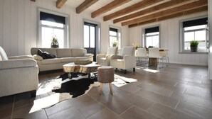 A spacious living room with a high ceiling, wooden beams, a large window, a sofa, chairs, a coffee table, and a cowhide rug. - Family Home in Rural Location near Coast of Noord-holland Province (Callantsoog)