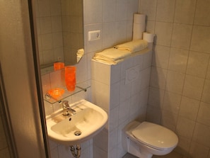 A bathroom with a white sink, a toilet, and a glass shelf holding orange cups.