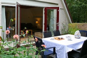 An outdoor dining area with a table set for two, chairs, and a chessboard.