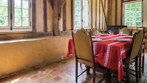 Uma sala de jantar com toalha vermelha, cadeiras de madeira e grandes janelas com vista para o verde.