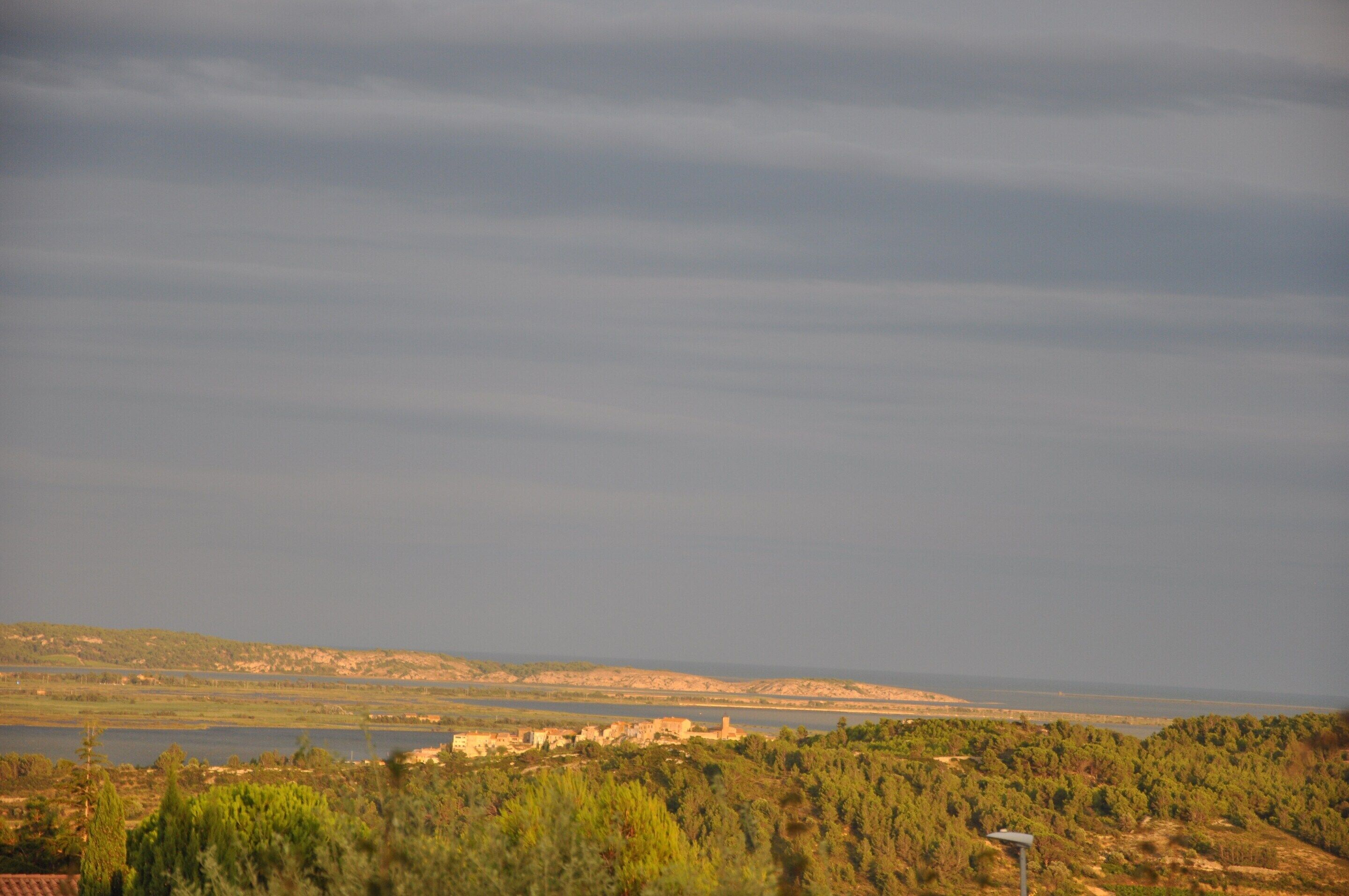 A landscape view with a body of water, distant buildings, and a cloudy sky.