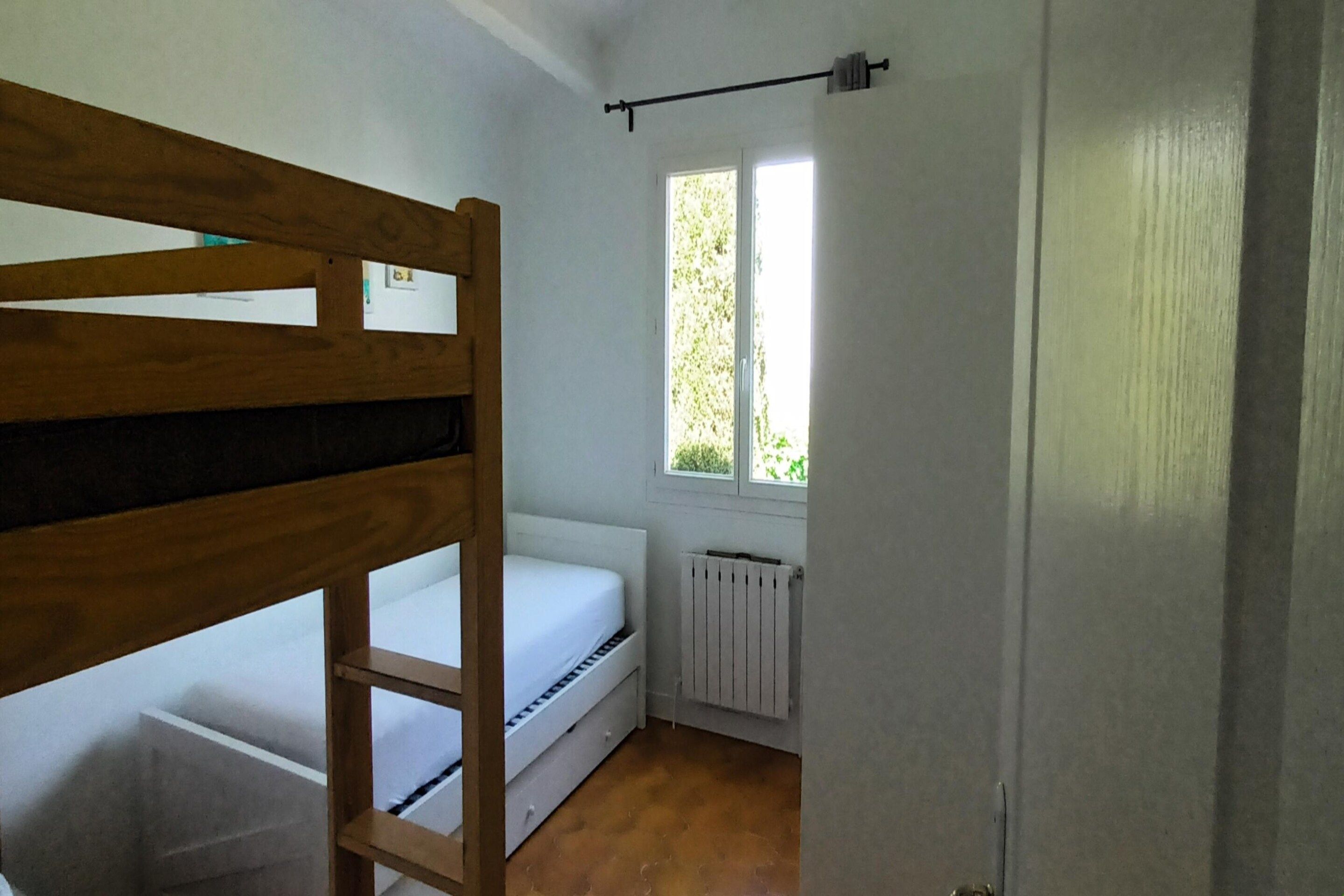 Un petit logement composé d’une seule pièce, avec un lit superposé, une fenêtre et un radiateur.