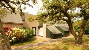 A building with a brick facade, a green-roofed structure, and a well-maintained lawn with flowering bushes. - Nice Holiday Home for 5 People, Within Walking Distance of the Beach (Burgh-Haamstede)