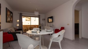 Ein Essbereich mit einem runden Tisch, weißen Stühlen und einem roten Stuhl. Im Hintergrund befindet sich eine Couch und ein kleiner Tisch mit einer Lampe.