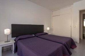 A bedroom with two beds, a white nightstand, a black headboard, and a white wardrobe. - Mare Verde 95 - One Bed (Costa Adeje)
