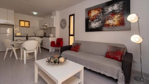 Ein modernes Wohnzimmer mit einem grauen Sofa, einem weißen Couchtisch und einem roten Sessel. An der Wand hängt ein Gemälde und ein Stehlampen steht dort.