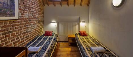 A cozy room with two beds, a wooden floor, a brick wall, a skylight, and a round light fixture.
