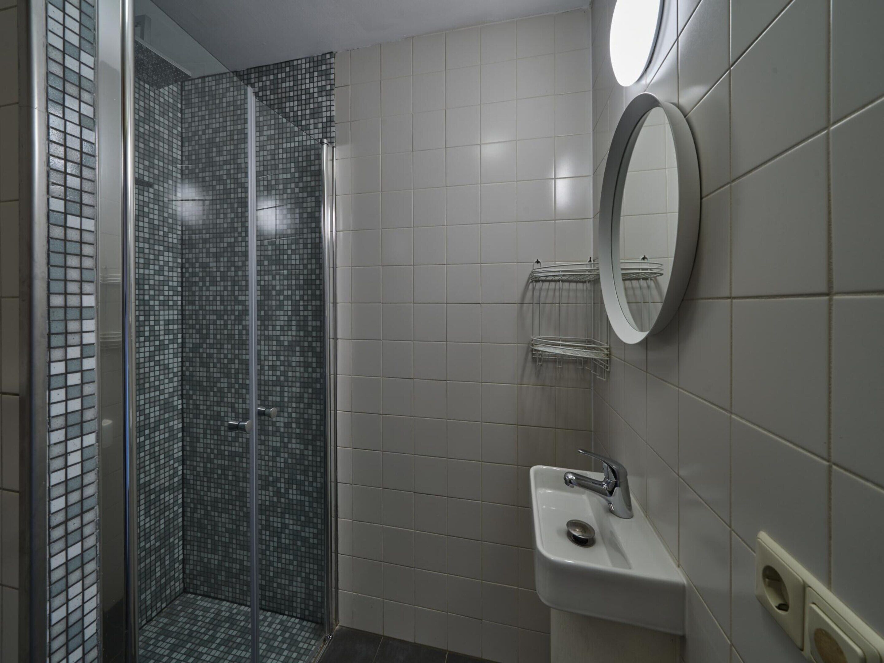 Une salle de bain avec une douche à parois de verre, un lavabo avec un miroir et des murs carrelés.