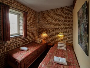 A room with two beds, brick walls, a window with curtains, and a painting on the wall. - Spacious Apartment near Town Center in Mesch (Eijsden)