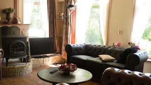 Uma sala de estar acolhedora com lareira, um sofá, uma mesa de centro com flores e uma televisão.