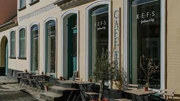 A café with outdoor seating, a cobblestone street, and a building with arched windows.