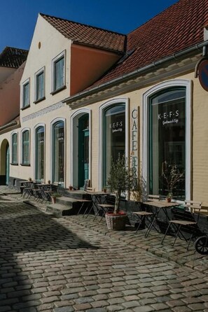 Un café con terraza, una calle adoquinada y un edificio con ventanas de arco.