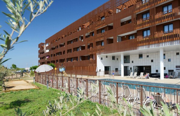 Ein mehrstöckiges Hotel mit Poolbereich, Außenbereich und überdachter Eingangszone.