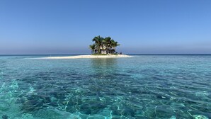 Ein tropischer Strand mit klarem türkisblauem Wasser, einer kleinen Insel mit Palmen und einer mit Reet gedeckten Hütte.