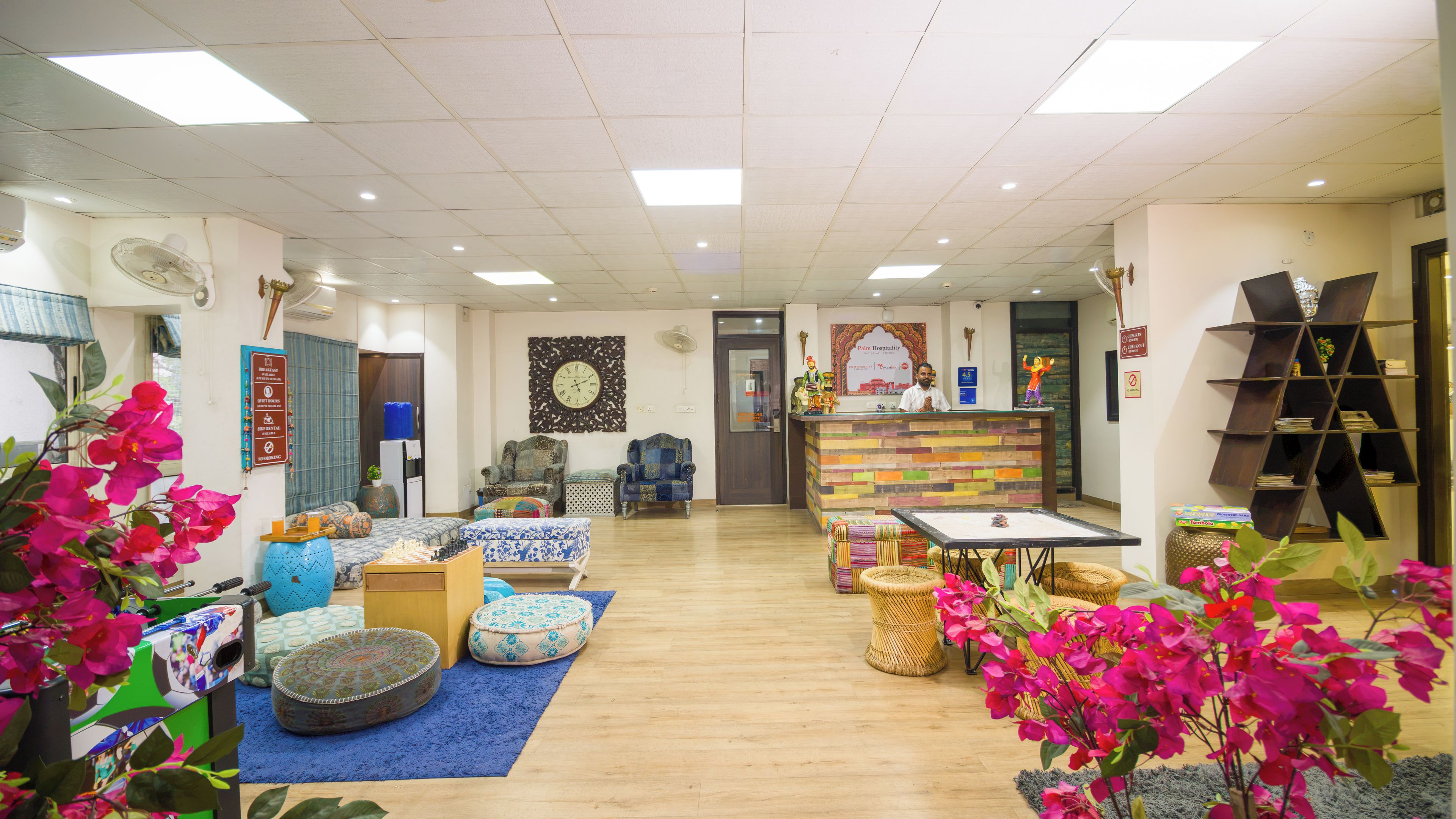 A hotel lobby with a reception desk, seating area with armchairs and ottomans, a large decorative wall, and a wooden floor.
