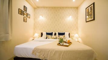 Quarto de hotel com uma cama grande, duas luminárias de cabeceira, um suporte com uma planta e papel de parede estampado.