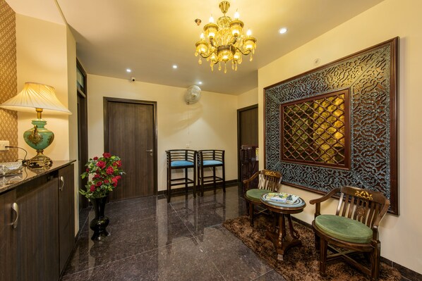 A well-lit hallway with a chandelier, two chairs, a table, and a decorative wall panel. - House of Backpackers (Jaipur)