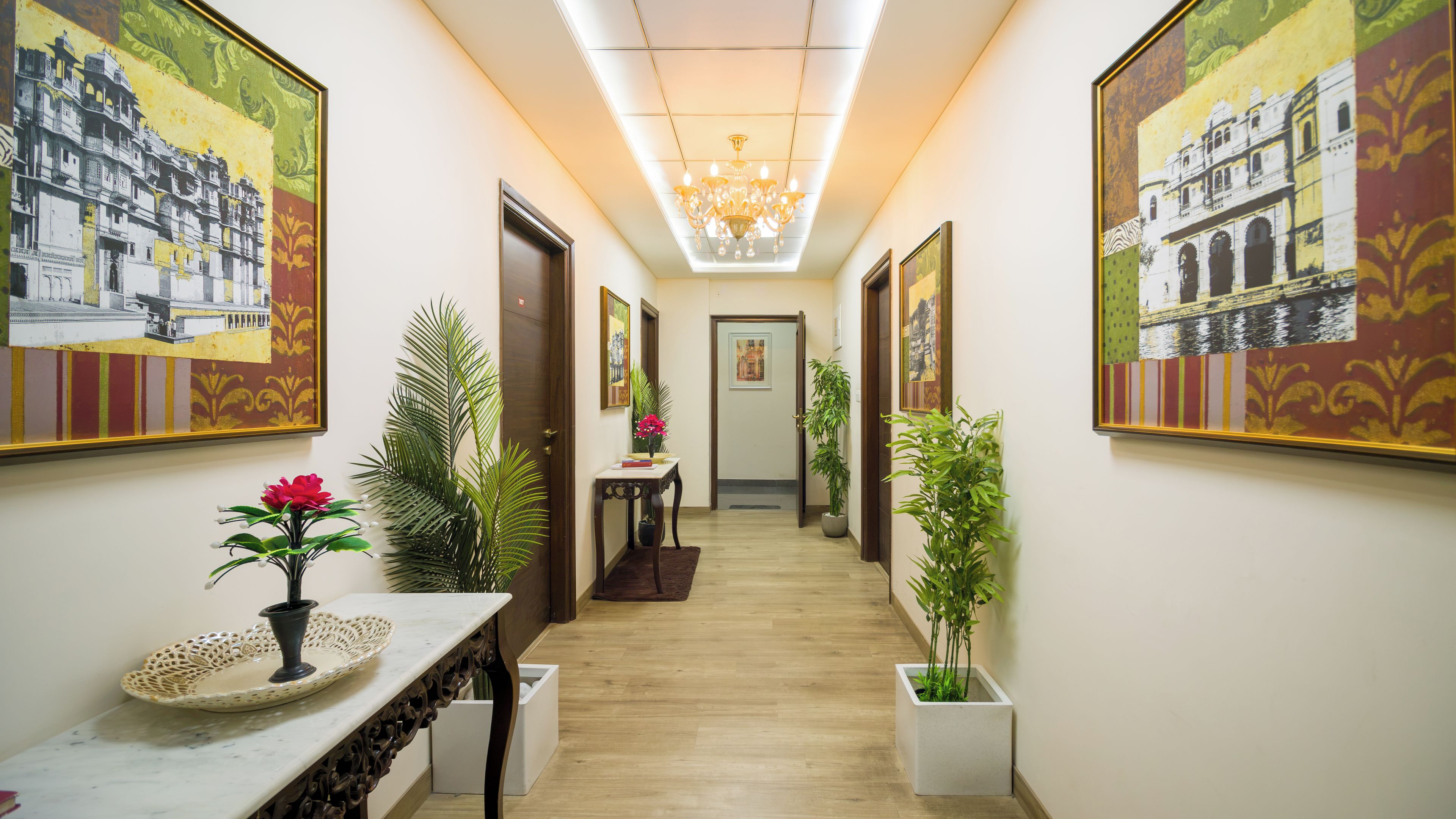 A hallway with artwork on the walls, a table with a vase of flowers, and potted plants.
