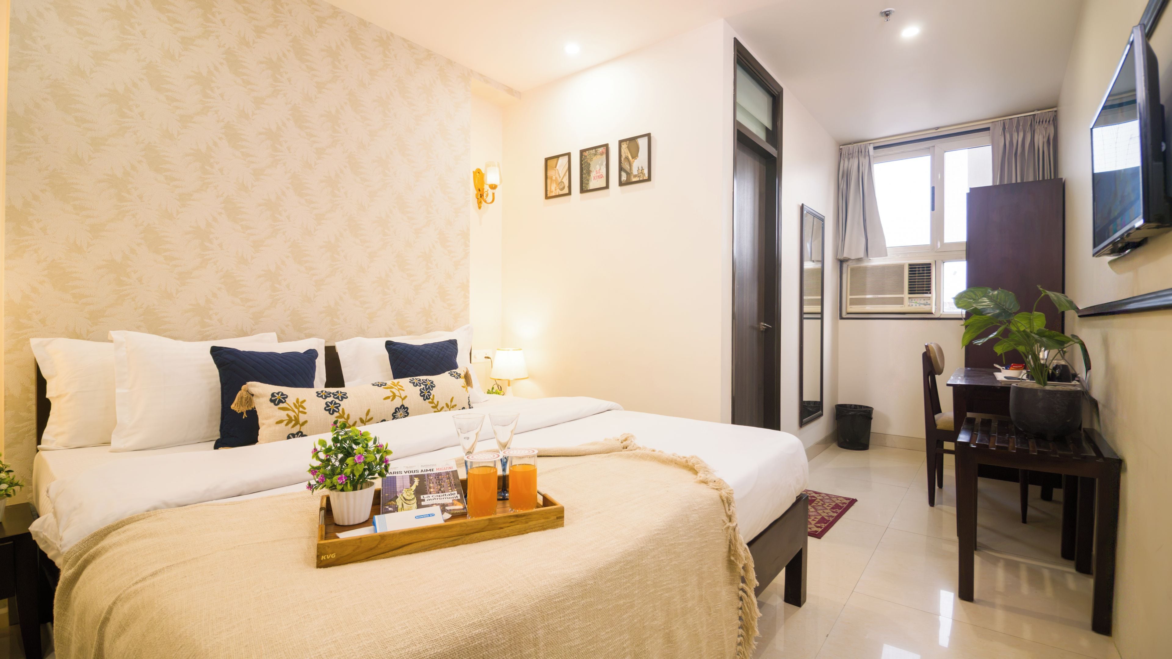 A hotel room with a bed, bedside table, lamp, wall art, and a desk with a chair.