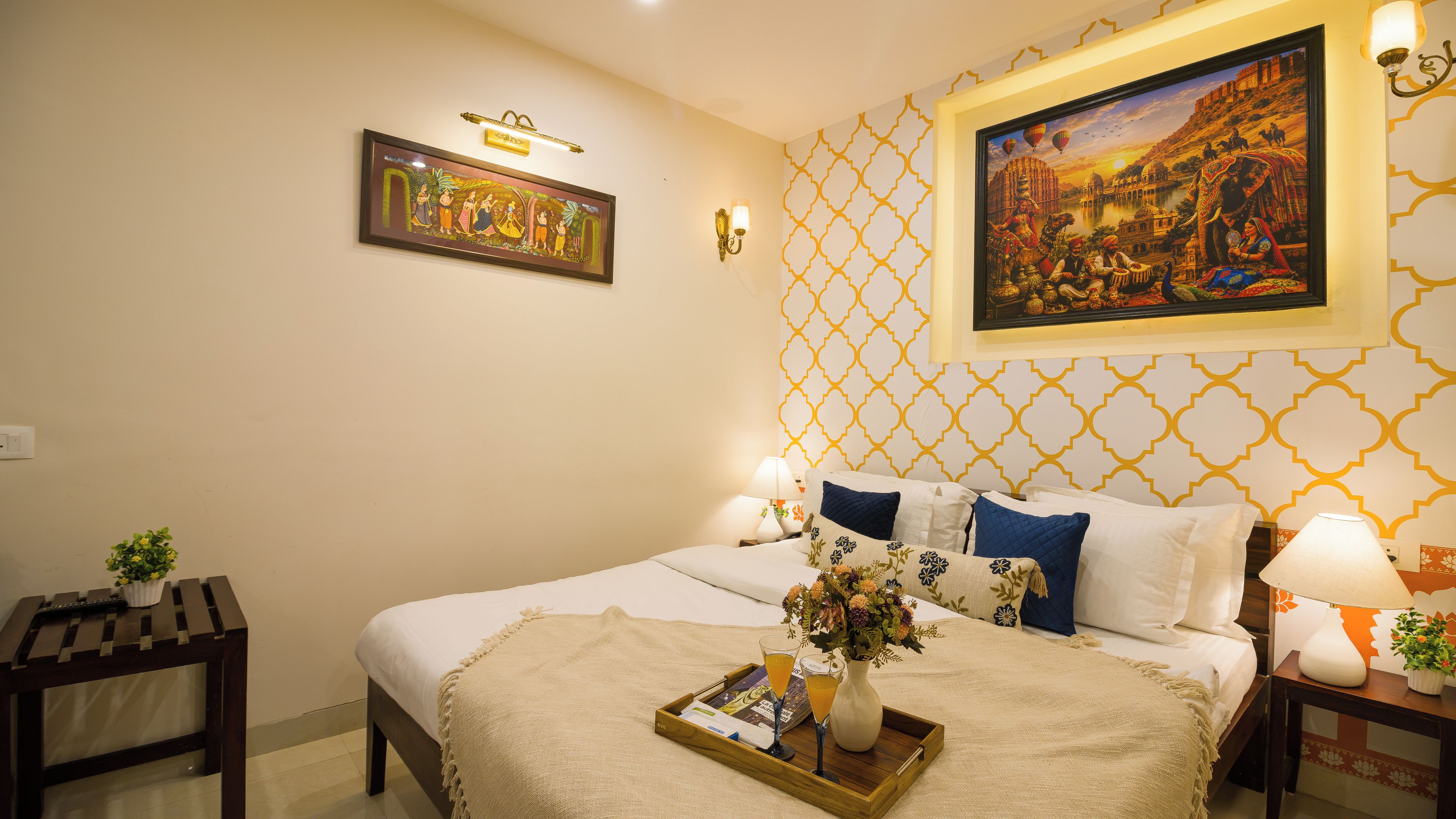 A hotel room with a bed, a nightstand, a wall-mounted lamp, a framed picture, and a decorative wall pattern.