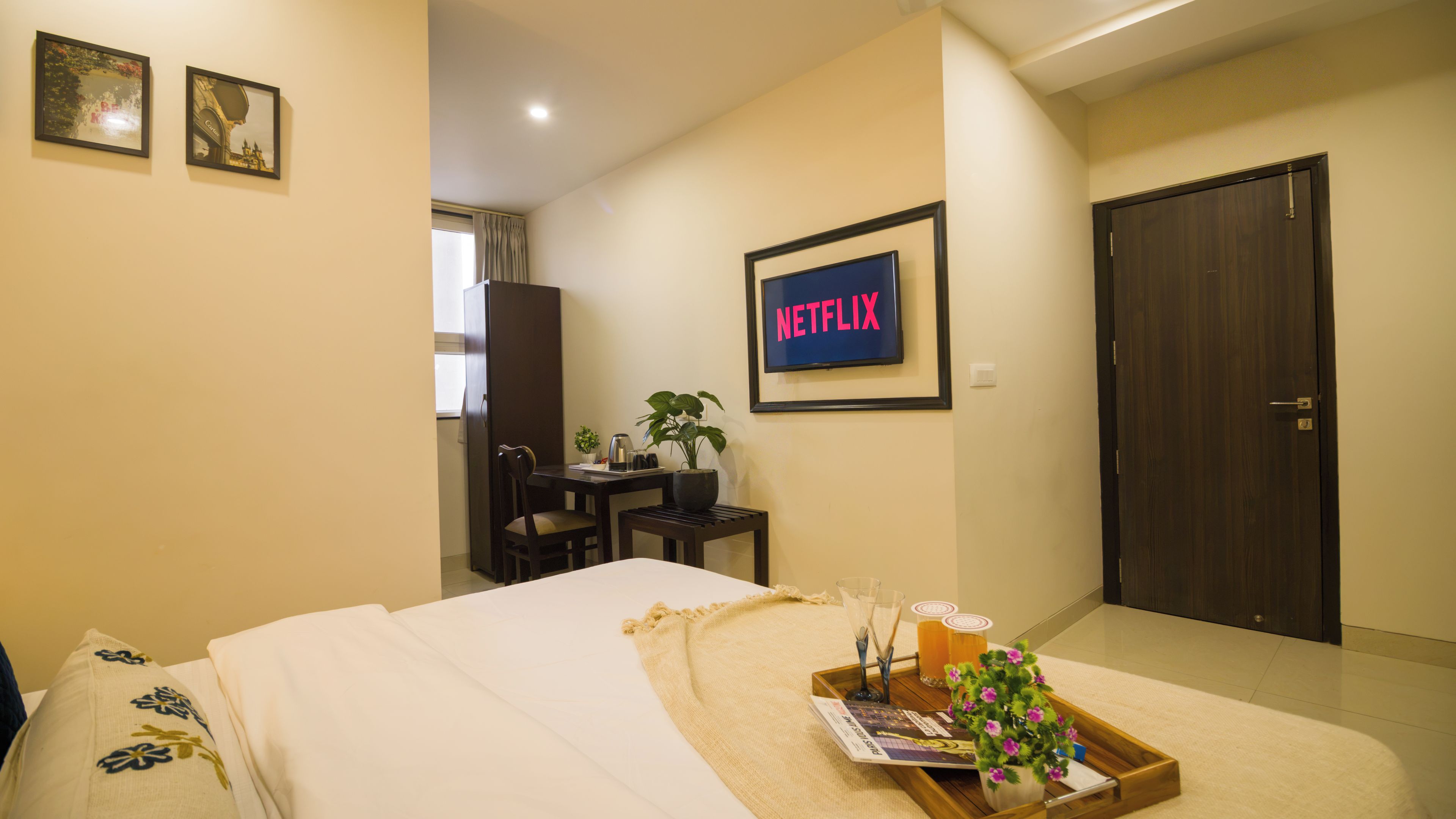 A hotel room with a bed, a desk, a chair, a TV displaying 'NETFLIX', and a door.
