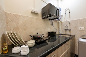 A kitchen with a stove, a microwave, and a toaster. There are plates, bowls, and a bottle on the counter. - House of Backpackers (Jaipur)
