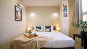A hotel room with a bed, bedside lamps, a nightstand, a tray with items, and a window with curtains. - House of Backpackers (Jaipur)