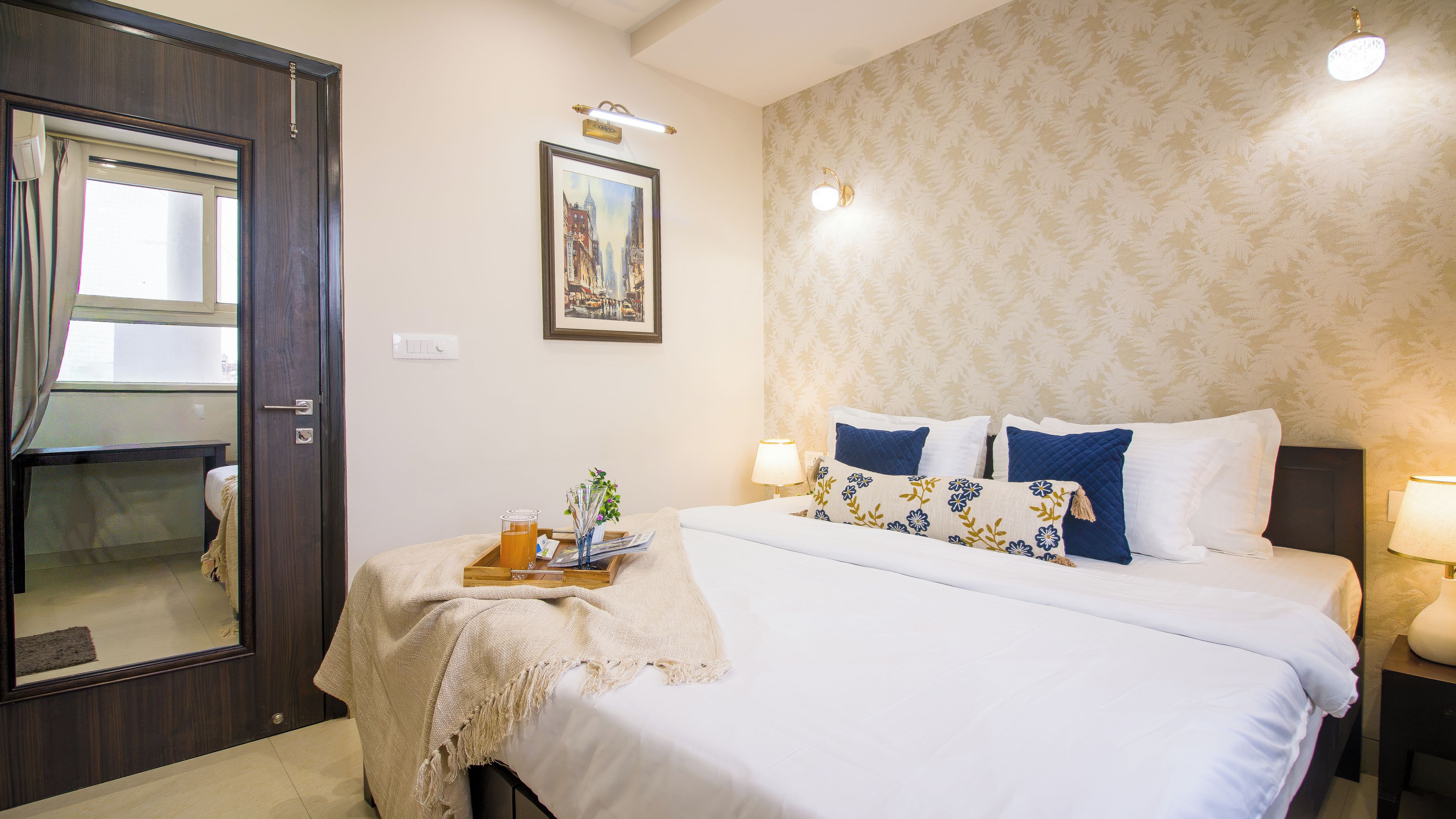A hotel room with a bed, bedside table, lamp, and a painting on the wall.