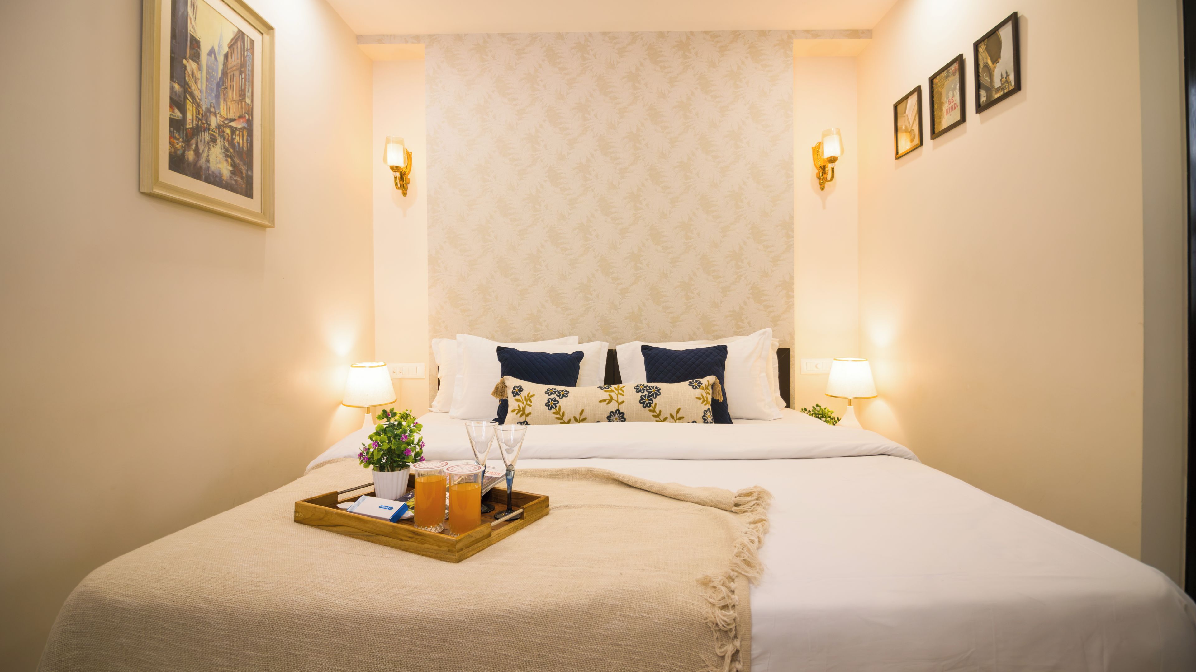 Habitación de hotel con una cama grande, dos lámparas de noche, una bandeja con una bebida y un vaso, y un cuadro en la pared.