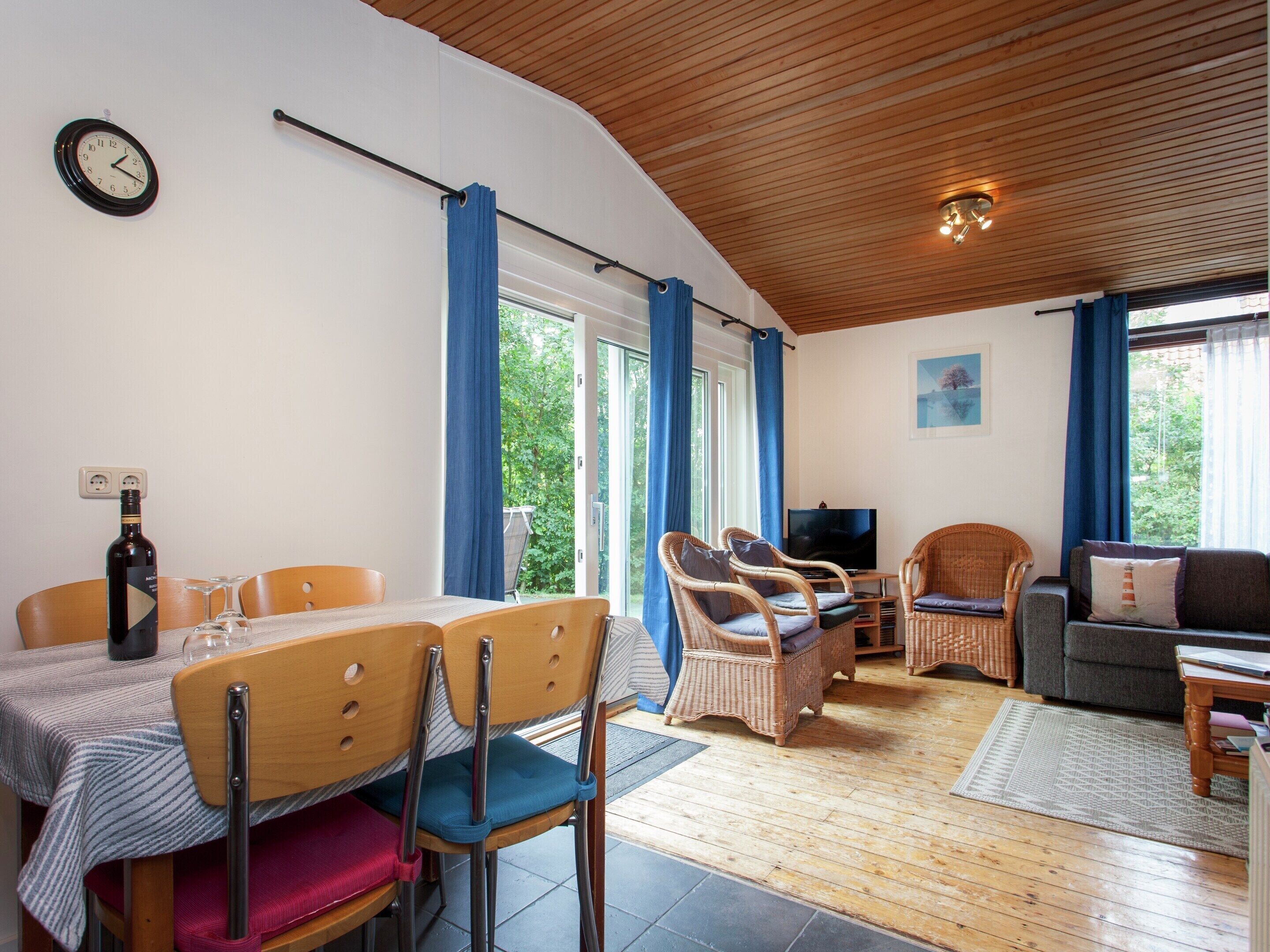 Ein gemütliches Wohnzimmer mit Essbereich, Holzböden und großen Fenstern mit blauen Vorhängen.