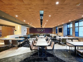 A modern dining area with multiple tables and chairs, a wooden ceiling, and large windows.