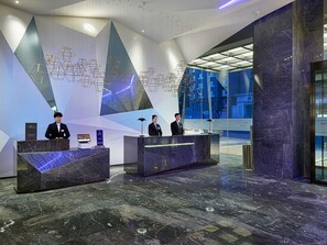 En moderne hotellobby med skranker i marmor, geometrisk vægkunst og store vinduer.