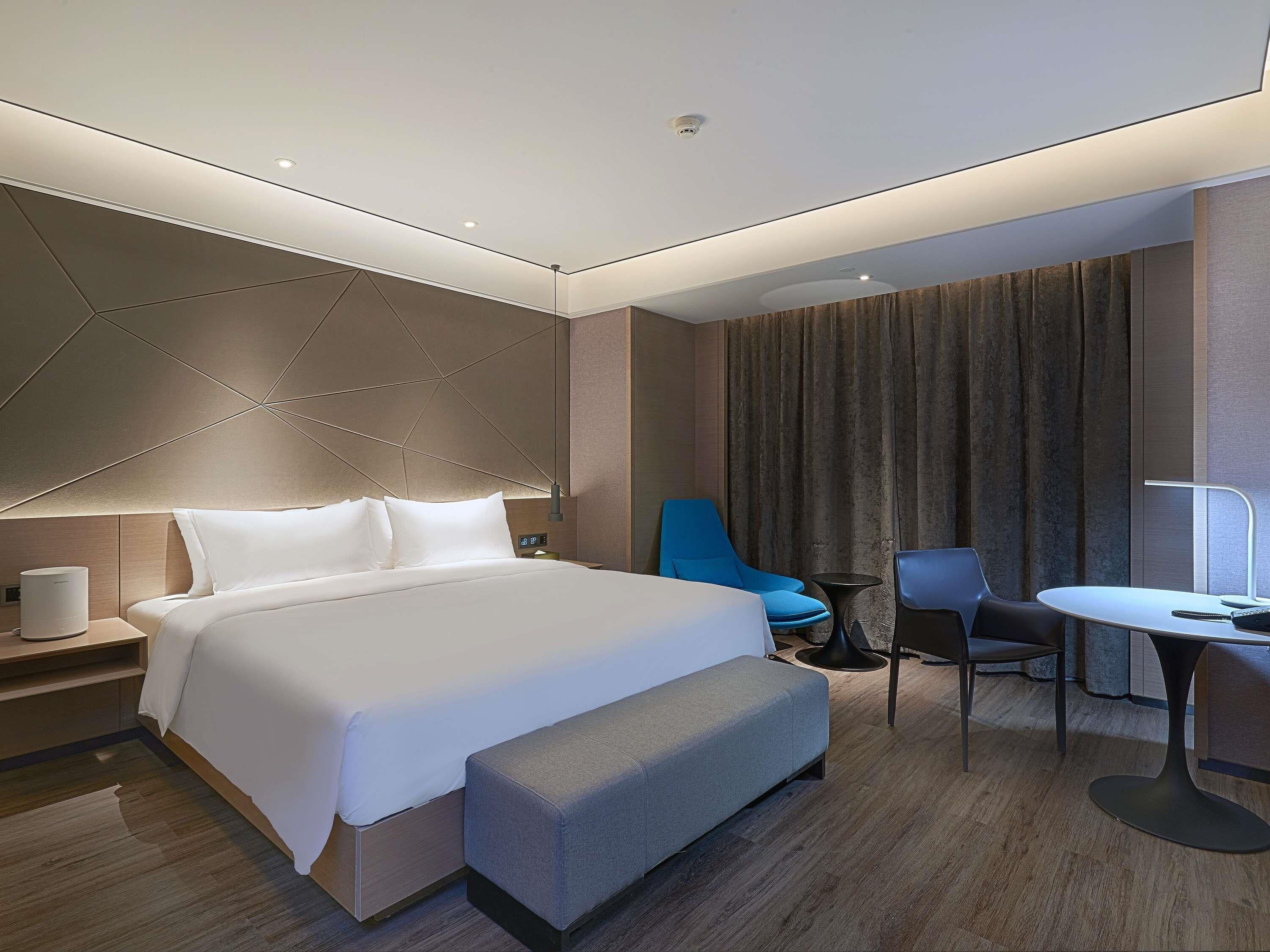 Ein modernes Hotelzimmer mit einem großen Bett, einem Schreibtisch, einem Sessel und einem kleinen Tisch.